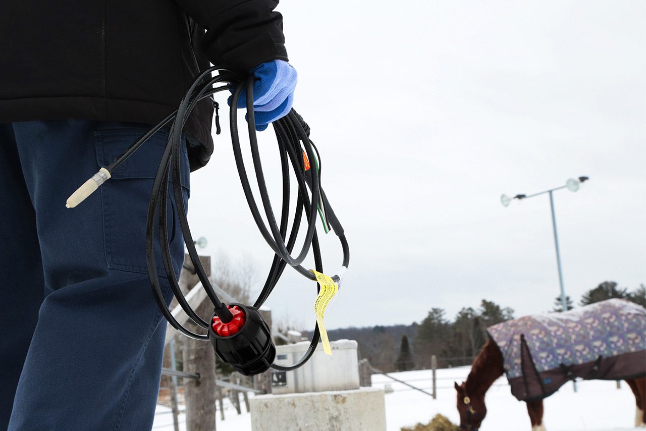Contractor holding Rizer-Line self-regulating heating cable outdoors at farm beside horse